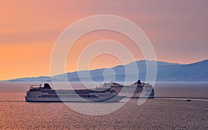 Two big tourist cruise liners manoeuvre in harbor. Beautiful sunset sky and distant hazy islands. Sea voyage, comfort