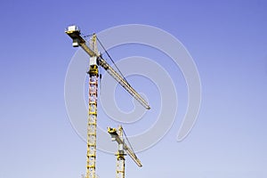 Two big yellow construction cranes on blue sky background