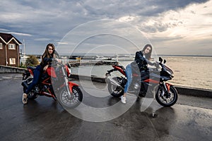 Two Biker girls in leather jackets on a black and red color sport motorcycles