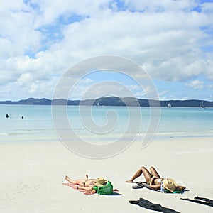 Two bikini clad girls sunbathing on white beach