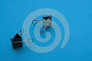 Two binder clips close up on a blue background depict characters holding out their hands to each other, selective focus
