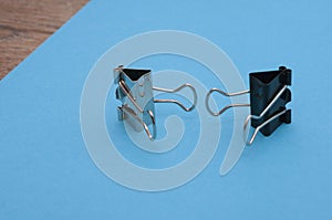 Two binder clips close up on a blue background depict characters holding out their hands to each other, selective focus