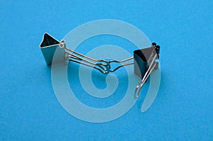 Two binder clips close up on a blue background in the image of characters holding hands, selective focus
