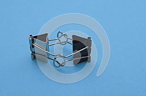 Two binder clips close up on a blue background in the image of characters holding hands, selective focus