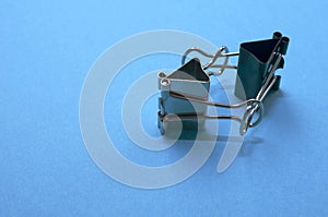 Two binder clips close up on a blue background in the image of characters holding hands, selective focus