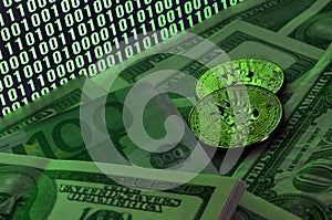 Two bitcoins lies on a pile of dollar bills on the background of a monitor depicting a binary code of bright green zeros and one u