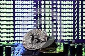 Two bitcoins lies on a videocard surface with background of screen display of cryptocurrency mining by using the GPUs