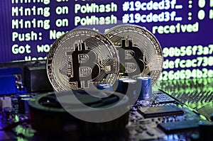 Two bitcoins lies on a videocard surface with background of screen display of cryptocurrency mining by using the GPUs