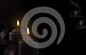 Two black burning candles on black background with waved ribbons
