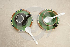 Two black ceramic cups for coffee on green saucers with spoons