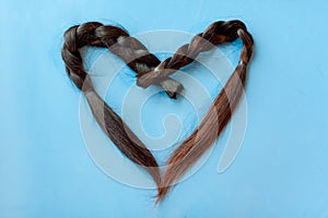 Two black chopped-off braids of human hair in a heart shape