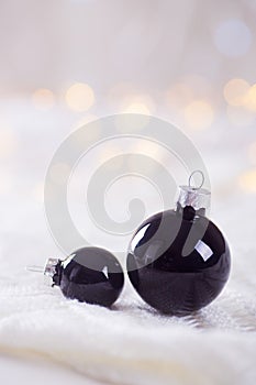 Two black Christmas balls on white lace on light and warm bokeh