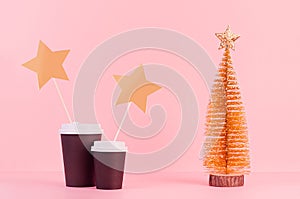 Two black coffee paper cups mock up with golden Christmas tree and blank sticker on pink background, template for advertising.