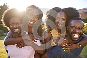 Two black couples, men piggybacking their partners, close up