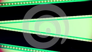 Two black film strips on pink background illuminated with green neon light, close up. Copy space.