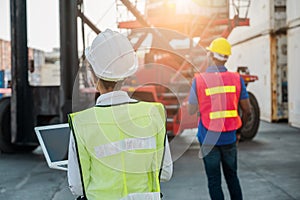 Two Black foreman man & woman worker working checking at Container cargo harbor holding laptop computer and using walkie-talkie to