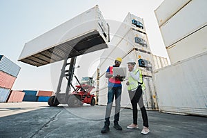 Two Black foreman man & woman worker working checking at Container cargo harbor holding laptop computer and using walkie-talkie to