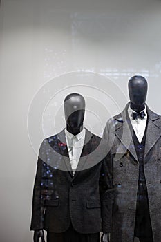 Two black male mannequins in dark suits and coats on a shop window with bokeh from festive lights