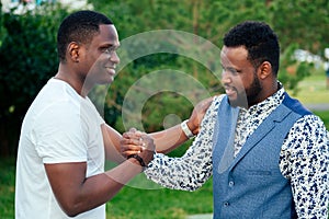 Two black men in stylish suits meeting in a summer park. African-Americans friends hispanic businessman greeting each