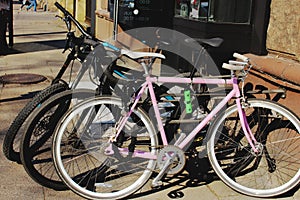 Two black and a pink bicycle parked on city street