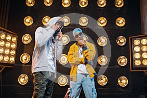 Two black rappers in caps on stage with spotlights