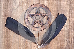Two Black Raven feathers and Wooden encircled Pentagram symbol on wood. Five elements: Earth, Water, Air, Fire, Spirit.