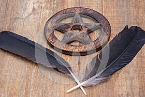 Two Black Raven feathers and Wooden encircled Pentagram symbol on wood. Five elements: Earth, Water, Air, Fire, Spirit.