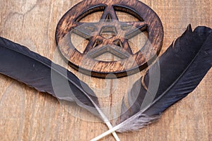 Two Black Raven feathers and Wooden encircled Pentagram symbol on wood. Five elements: Earth, Water, Air, Fire, Spirit.