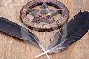 Two Black Raven feathers and Wooden encircled Pentagram symbol on wood. Five elements: Earth, Water, Air, Fire, Spirit.