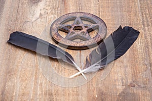 Two Black Raven feathers and Wooden encircled Pentagram symbol on wood. Five elements: Earth, Water, Air, Fire, Spirit.