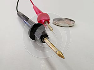 two black and red battery tester cables with a 3 volt button battery on a white table photo