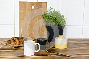 Two black and white espresso coffee cups, fresh baked croissant on kitchen table, counter, utensils dishware, home green