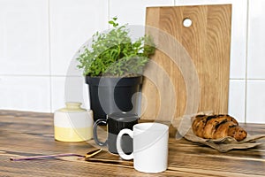 Two black and white espresso coffee cups,fresh baked croissant on kitchen table, counter,utensils dishware,home green