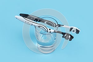 Two black and white toothbrush on a glass with mouthwash on blue background with copy space