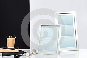 Two blank frames, paper cup of coffee on books and magnifier on tabletop against black and white studio background