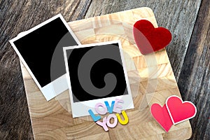 Two blank instant photos with red hearts. On wooden background