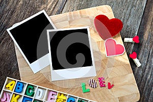 Two blank instant photos with red hearts. On wooden background