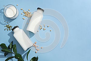 Two blank label bottles and a glass cup filled with milk displayed with green beans, soybeans and peanuts