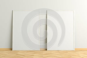 Two blank vertical posters. frame mock up standing on light herringbone parquet floor next to white wall.