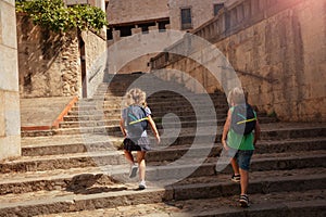 Two blond kids walk in Girona, go up stairs at historical part