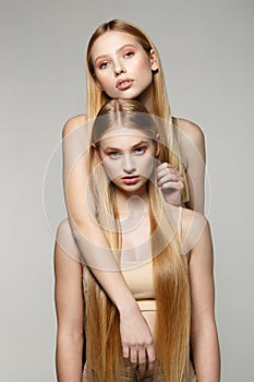 Two blonde beautiful girls with long hair looking at camera in the studio on a bright background