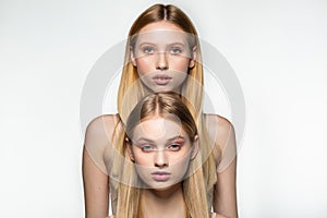 Two blonde beautiful girls with long hair looking at camera in the studio on a bright background, standing one by one