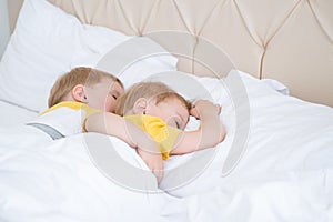 two blonde boys twins sleeping hugging on white bedding