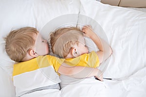 two blonde boys twins sleeping hugging on white bedding