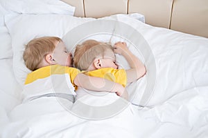 two blonde boys twins sleeping hugging on white bedding