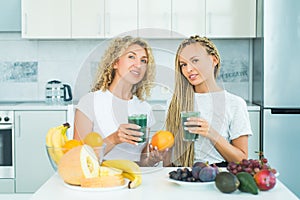 Two blonde healthy girls friends drinks green smoothie. Fitness and dieting. Food supplements. Weight loss. Glass is