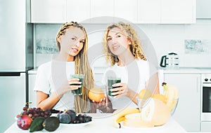 Two blonde healthy girls friends drinks green smoothie. Fitness and dieting. Food supplements. Weight loss. Glass is