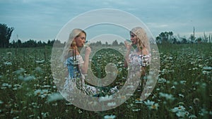 Two blondes sitting on the field and drinkind white wine