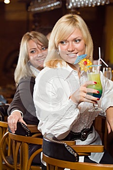 Two blonds at a bar counter with a cocktail