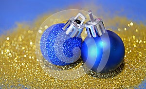 Two blue Christmas balls on golden glitter on blue background